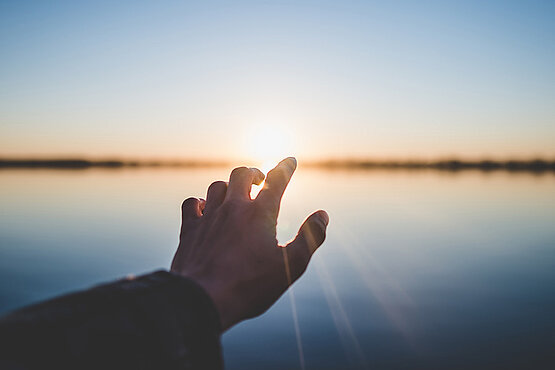 Silhouette einer Hand vor einem starahlenden Sonnenaufgang