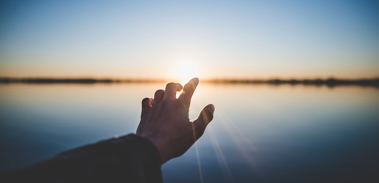 Silhouette einer Hand vor einem starahlenden Sonnenaufgang