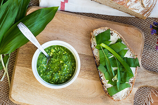 Küchenbrett mit frisch gemachtem Bärlauchpesto und Butterbrot garniert mit frischen Bärlauchblättern