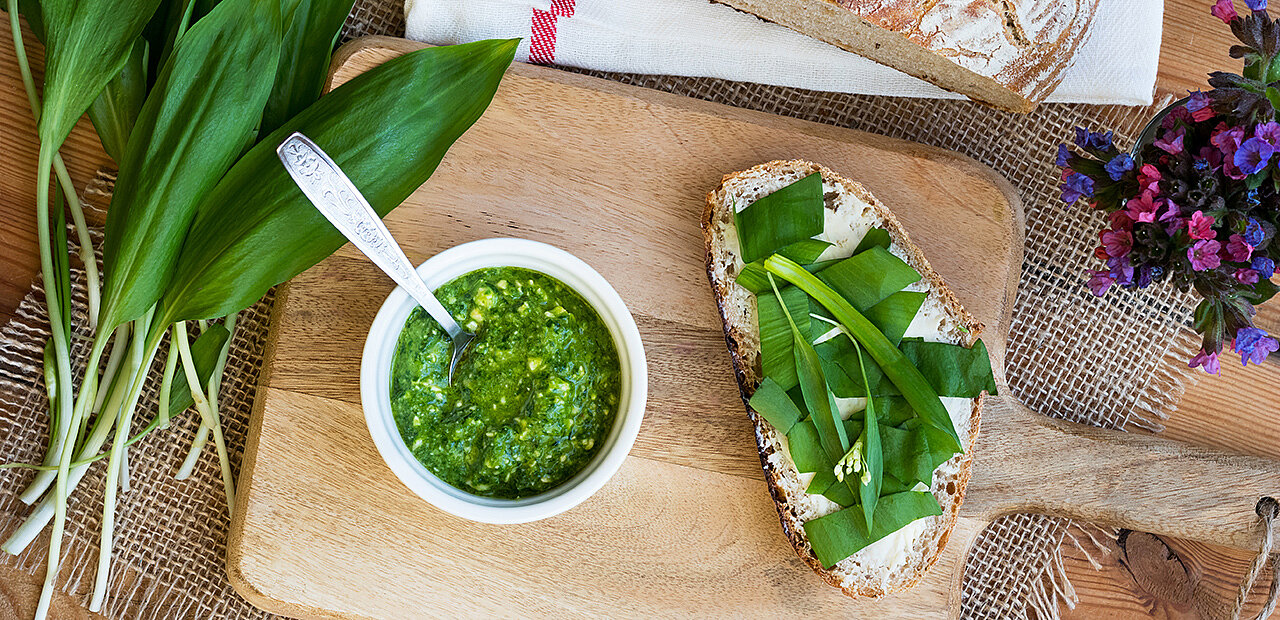 Küchenbrett mit frisch gemachtem Bärlauchpesto und Butterbrot garniert mit frischen Bärlauchblättern