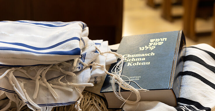 Auf einer Kirchenbank liegt ein Tallit und ein jüdisches Gebetsbuch.  