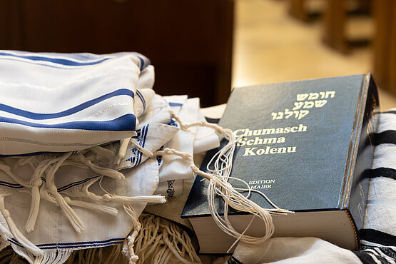 Auf einer Kirchenbank liegt ein Tallit und ein jüdisches Gebetsbuch.  