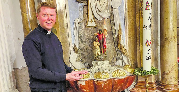 Pfarrer Clemens Beirer und einer seiner „Lieblingsorte“: der Taufbrunnen.