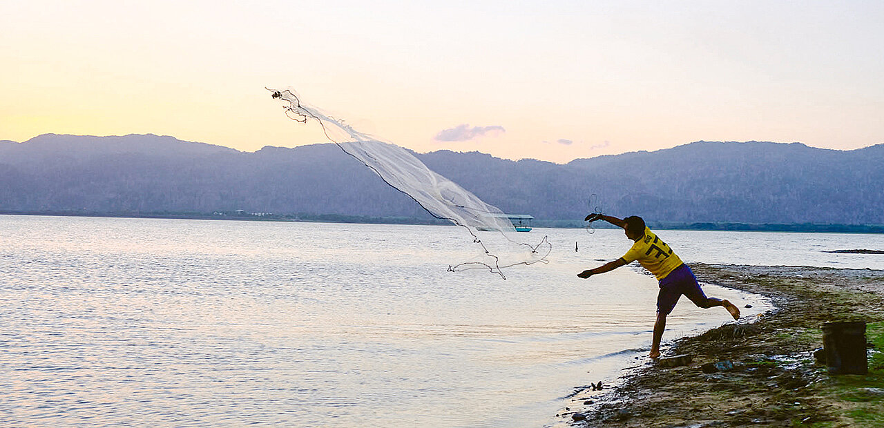 Ein Junger mann steht am Meeresrand und wirf ein Fischernetz aus.