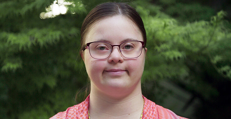 Eine junge Frau mit Down-Syndrom lächelt in die Kamera.