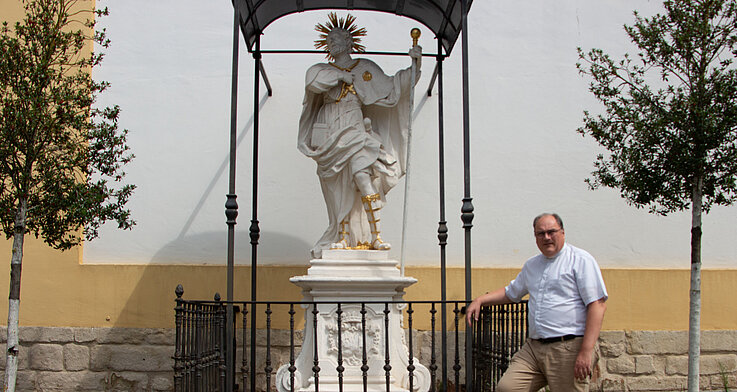 Pfarrer Andreas Kaiser neben der Statue des heiligen Koloman vor der Pfarrkirche Stockerau. 