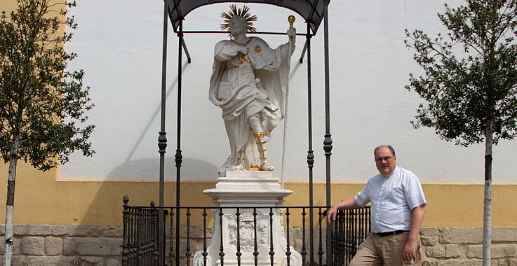 Pfarrer Andreas Kaiser neben der Statue des heiligen Koloman vor der Pfarrkirche Stockerau. 