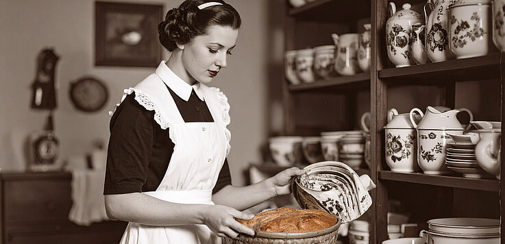 Symbolbild einer traditionellen Hausfrau mit Schürze wie in den 1950ern mit Brot