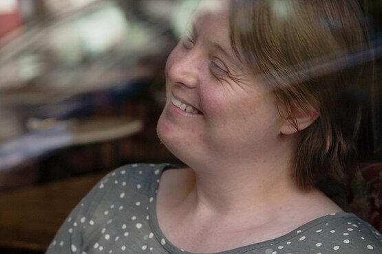 Eine Frau mit Down-Syndrom sitzt hinter einer Glasscheibe.
