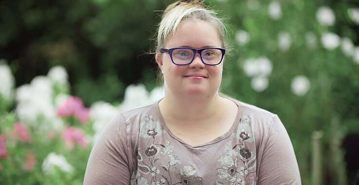 Eine Frau mit Down Syndom steht in einem Garten.