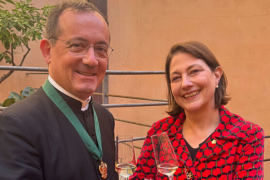 Rektor der Institution Santa Maria dell'Anima (links) mit Sophie Lauringer (rechts) auf der Terasse des Kollegs mit einem Glas Sekt in der Hand.