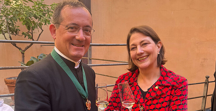 Rektor der Institution Santa Maria dell'Anima (links) mit Sophie Lauringer (rechts) auf der Terasse des Kollegs mit einem Glas Sekt in der Hand.