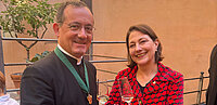 Rektor der Institution Santa Maria dell'Anima (links) mit Sophie Lauringer (rechts) auf der Terasse des Kollegs mit einem Glas Sekt in der Hand.