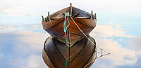 Ein kleines Holzruderboot, dass sich im Stillen Wasser spiegelt.