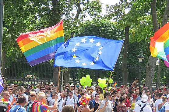 Regenbogenflaggen und eine EU-Flagge bei einer Demonstration.