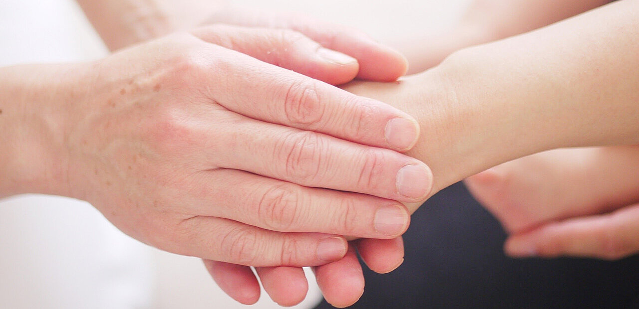 Hände halten eine weitere Hand. Im Hintergrund weitere Hände.