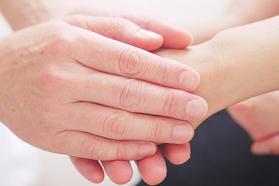 Hände halten eine weitere Hand. Im Hintergrund weitere Hände.