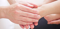 Hände halten eine weitere Hand. Im Hintergrund weitere Hände.