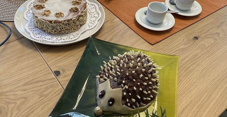 Tisch, gedeckt mit einer Nusstorte, Kaffeegeschirr und einem Marzipan-Igel.