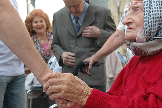 Alte Frau im Rollstuhl hält die Hand einer jüngeren Frau