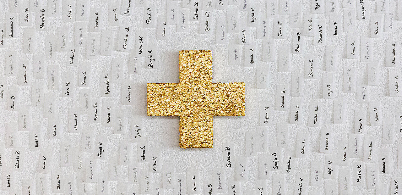 EIn gold glänzendes Kreuz umrahmt von mit unterschiedlichen Vornamen beschrifteten Papierstreifen