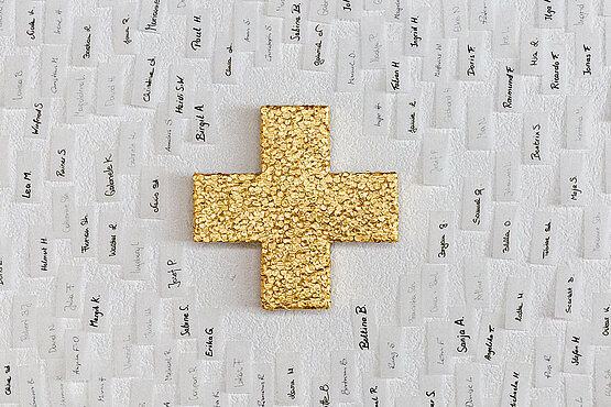 EIn gold glänzendes Kreuz umrahmt von mit unterschiedlichen Vornamen beschrifteten Papierstreifen