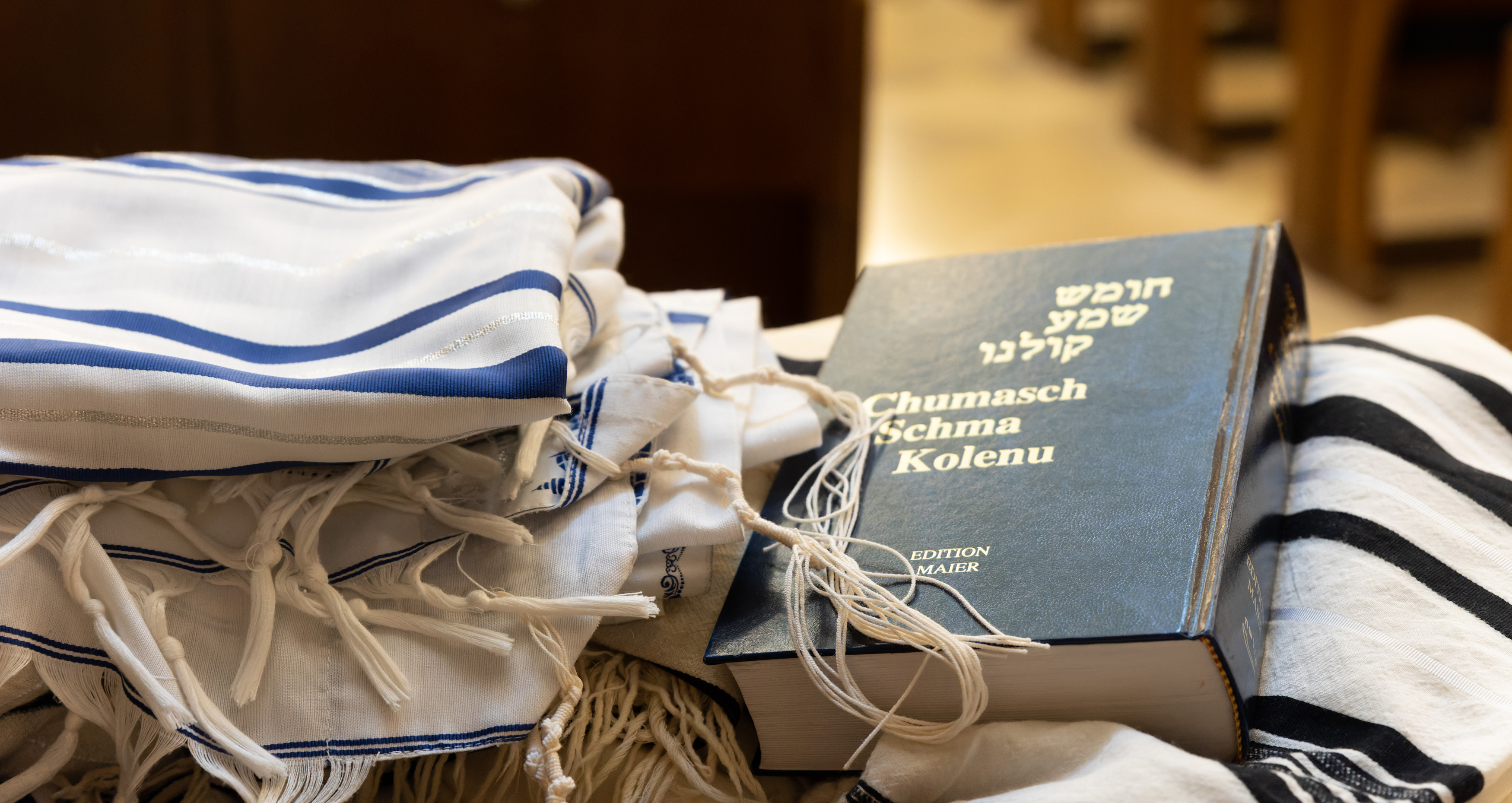 Auf einer Kirchenbank liegt ein Tallit und ein jüdisches Gebetsbuch.  